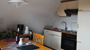 A compact kitchen with white cabinets, a black stove, and a wooden dining table. - Fewo Stricker 23 by Interhome (Walkenried)