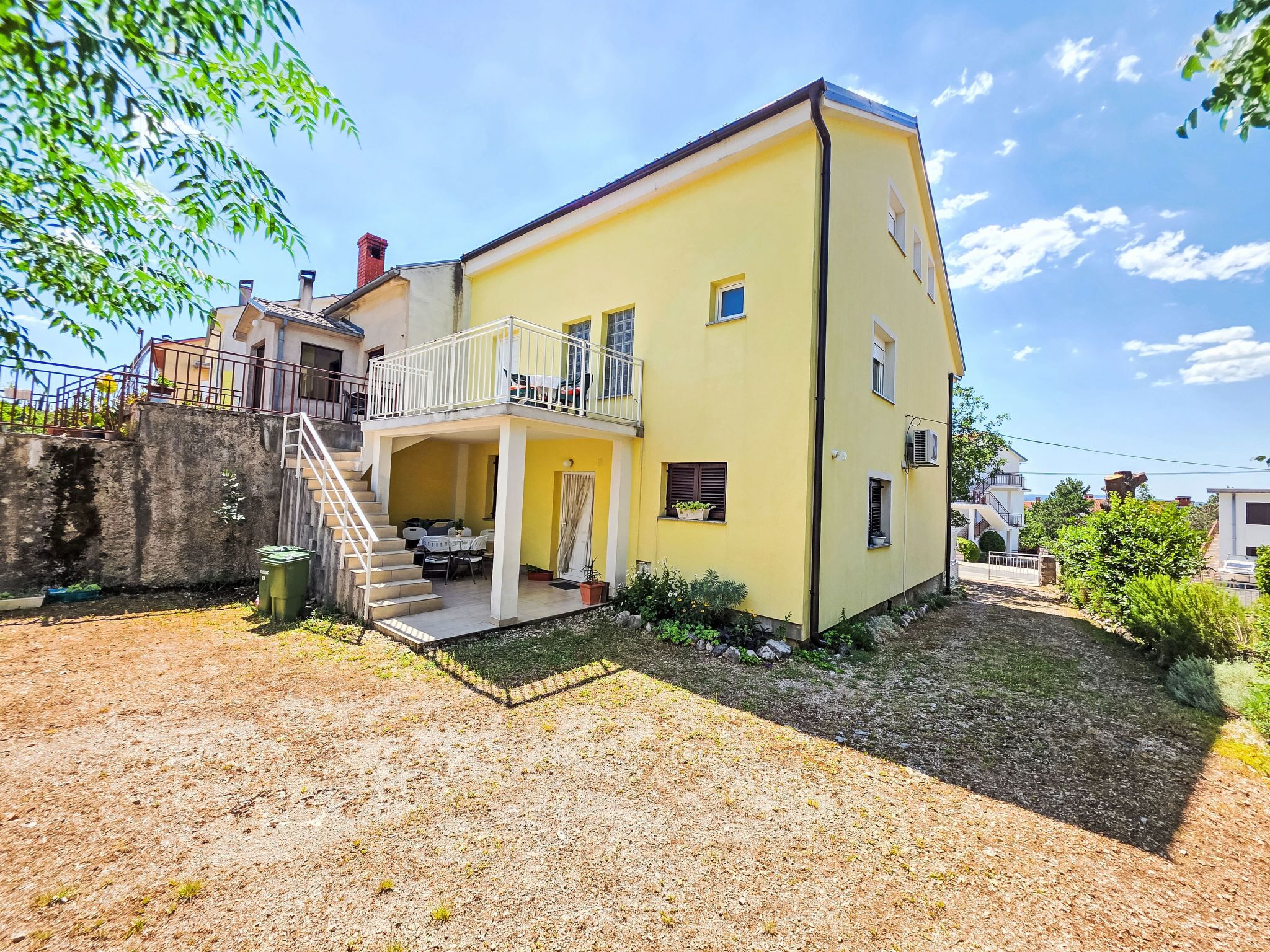 Un immeuble jaune à deux étages, doté d’un balcon, d’une terrasse couverte et d’un escalier menant à l’étage supérieur.