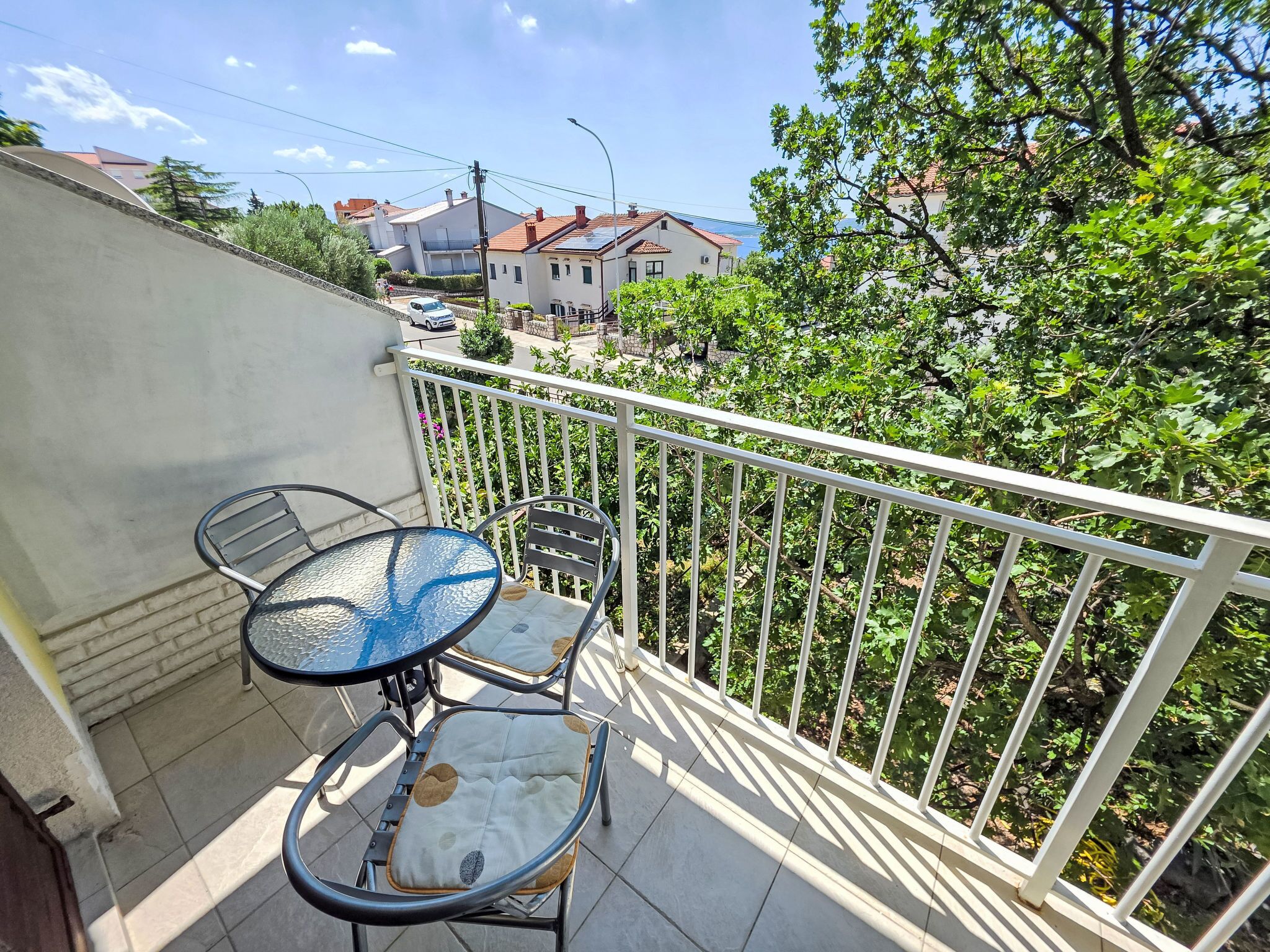 Un balcon avec une table et des chaises, une balustrade blanche et une vue sur des maisons et des arbres.