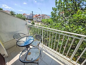 Ein Balkon mit Tisch und Stühlen, einem weißen Geländer und Blick auf Häuser und Bäume.