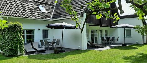 A house with a tiled roof, a covered patio with chairs and umbrellas, and a well-maintained lawn.