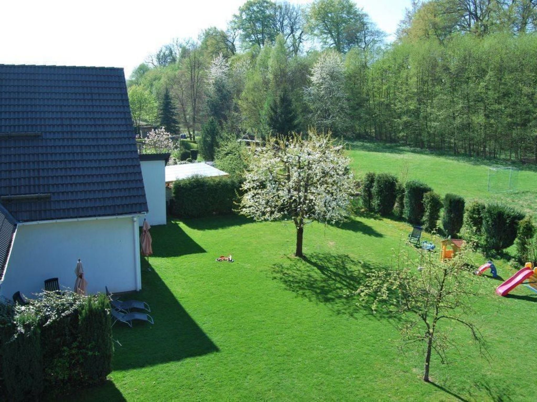 Ein Wohnhausgarten mit Rasen, Baum und Spielbereich inklusive Rutsche.