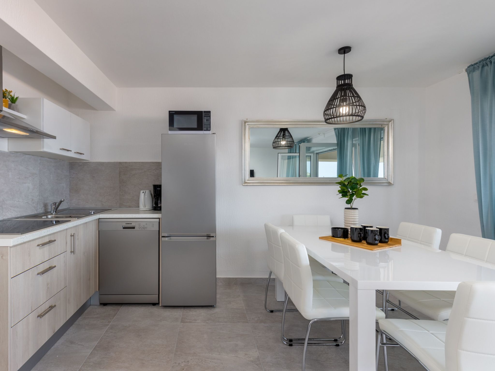 A modern kitchen with white cabinetry, a stainless steel refrigerator, a microwave, and a dining area with a white table and chairs.