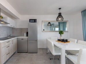Una cocina moderna con armarios blancos, un refrigerador de acero inoxidable, un microondas y un comedor con mesa y sillas blancas.