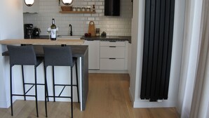 Moderni keittiö, jossa on keskeinen keittiösaareke, kaksi baarijakkaraa, kahvinkeitin ja viinipullo.