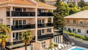 Un hotel de varios pisos con balcones, piscina y abundante vegetación.
