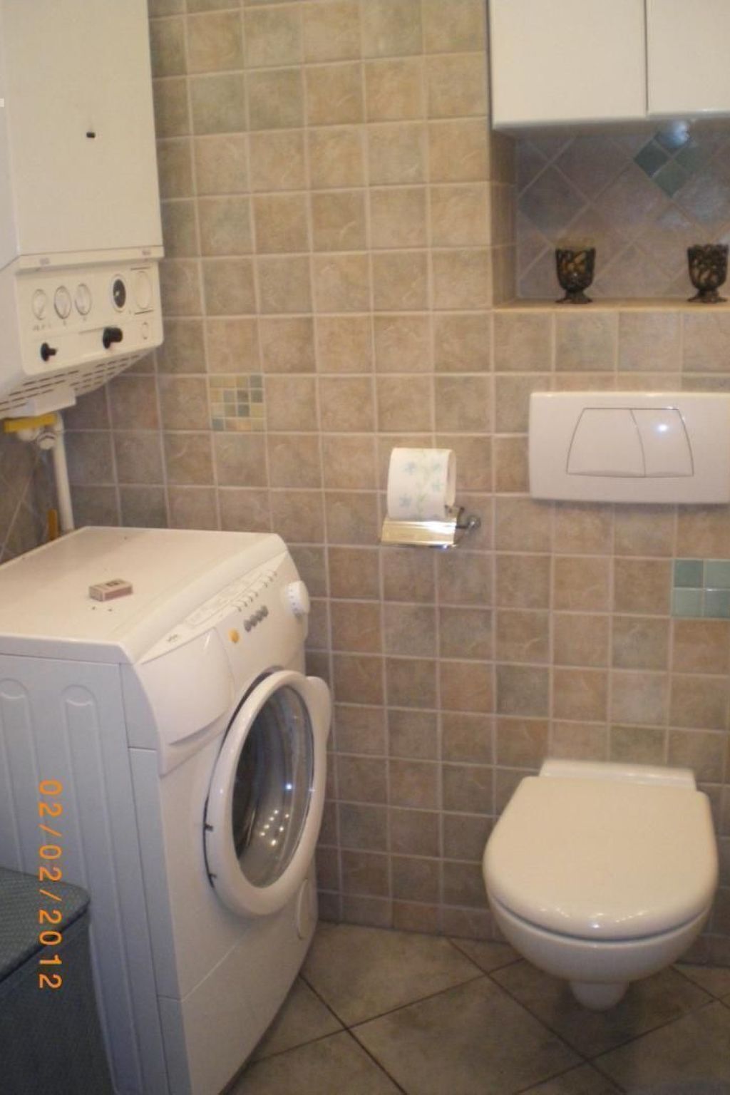 A compact bathroom with a washing machine, toilet, and tiled walls.