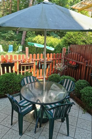 A patio with a glass table and chairs, surrounded by a wooden fence and greenery. - Charmantes Haus 100m vom Strand entfernt für 6 Personen by Interhome (Pobierowo)