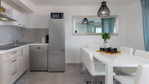 Eine moderne Küche mit weißen Schränken, einem Edelstahlkühlschrank, einer Mikrowelle und einem Essbereich mit weißem Tisch und Stühlen.