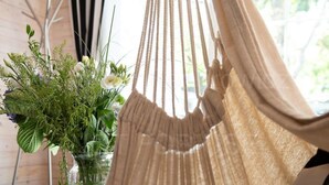 A hammock chair in a room with a wooden interior, a window with curtains, and a vase with flowers on a table. - Naval House am Spielplatz 2 by Interhome (Pobierowo)