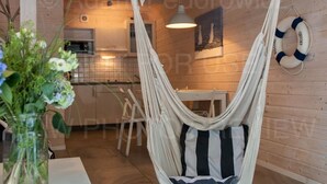 A hammock chair in a wooden interior space with a tiled floor, a white table with a vase of flowers, and a life ring on the wall. - Marine Cottages mit Hund by Interhome (Pobierowo)