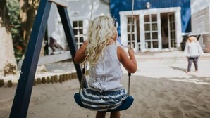 A child on a swing in a playground with a blue house in the background. - Marine Cottages mit Hund by Interhome (Pobierowo)