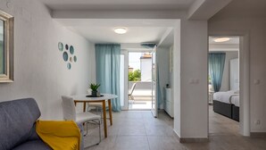 Una sala moderna con un sofá gris, una mesita con una planta y una mesa de centro. Hay un balcón con vistas al exterior.