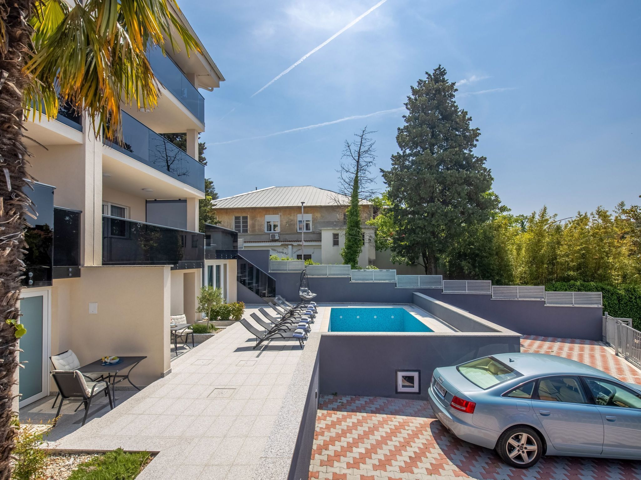 Un espace extérieur moderne doté d’une piscine, de chaises longues et d’une voiture garée à proximité.