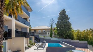 Un espacio exterior moderno con piscina, sillones de descanso y un coche aparcado cerca.