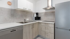 Una cocina moderna con armarios blancos, un refrigerador de acero inoxidable, un microondas y una cafetera.
