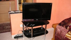 Un televisor sobre un soporte, con un control remoto, una regleta y un decodificador.