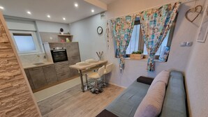 Un espacio habitable compacto con kitchenette, un comedor con mesa y sillas, y un sofá.