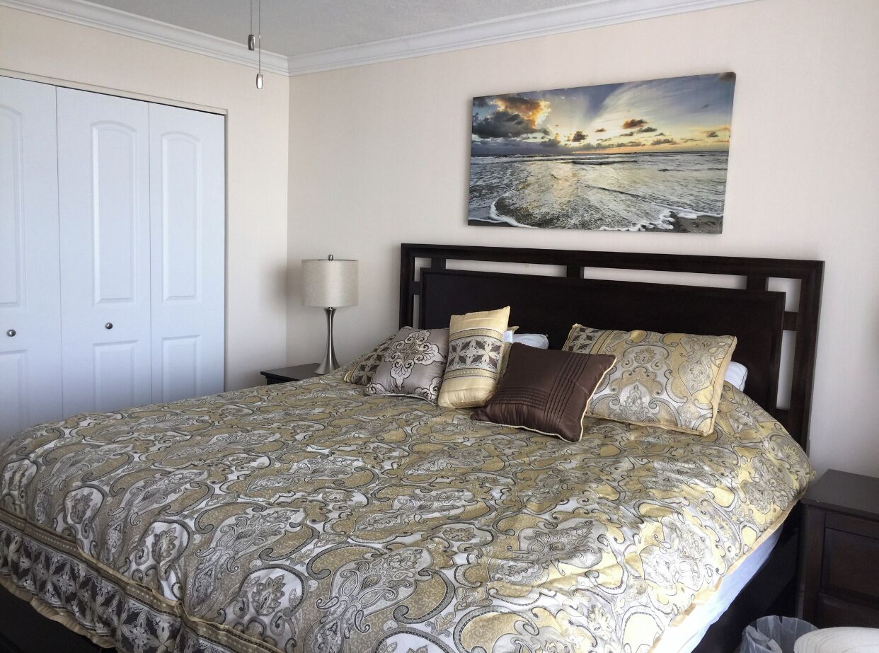 A bedroom with a large bed, a nightstand, a lamp, and a door.