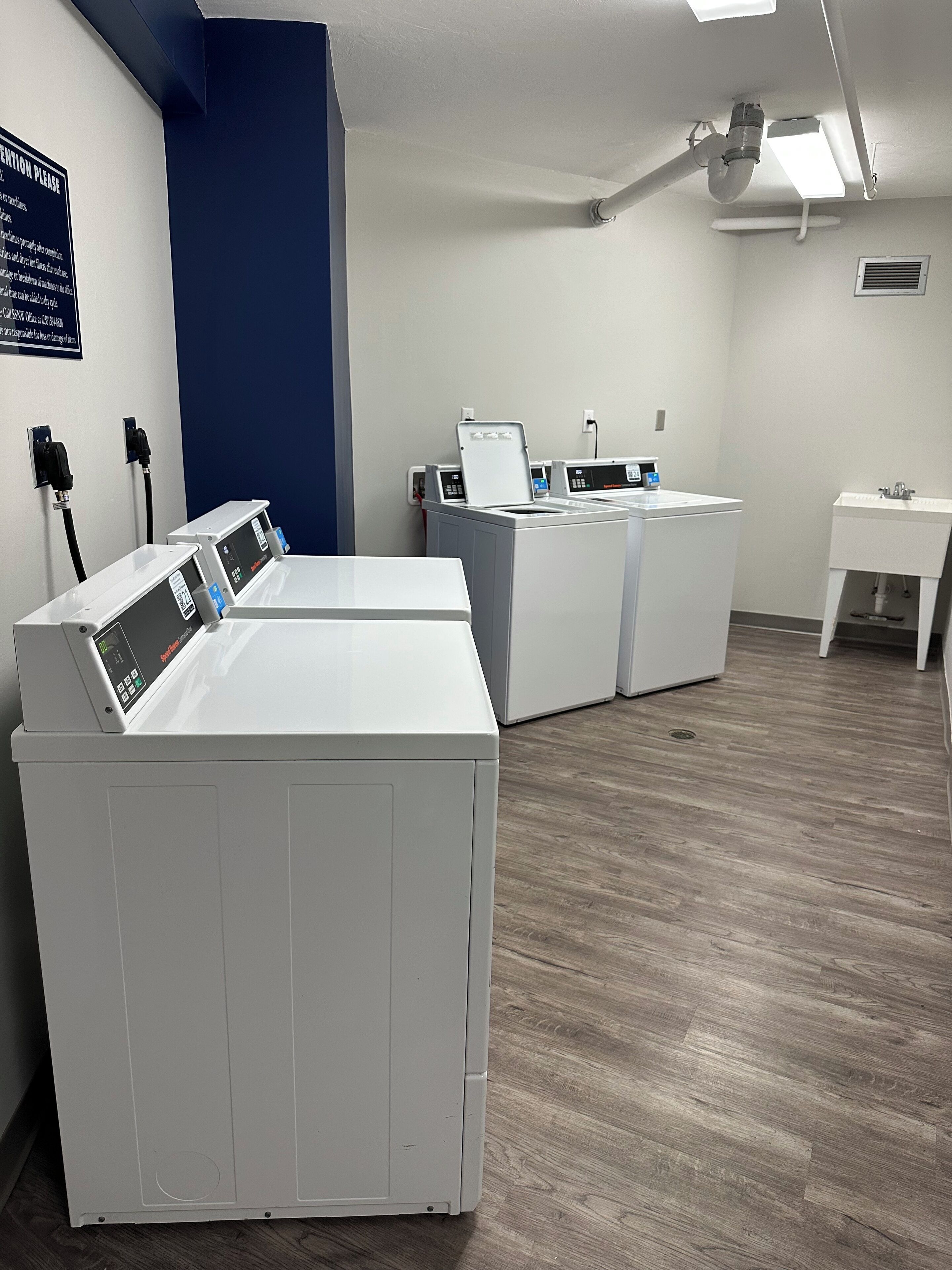 A laundry room with two front-loading washing machines, a sink, and a blue wall.