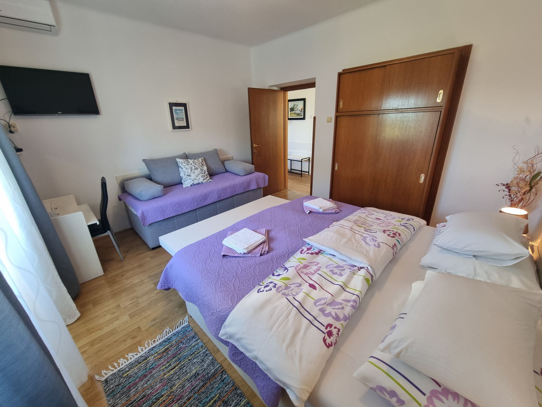 Um quarto com cama, sofá, escrivaninha e televisão.