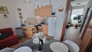 A modern kitchen with wooden cabinets, a microwave, and a refrigerator. There is a dining area with a table set for two, featuring white placemats and a vase with white flowers. - Wohnung 10m vom Strand entfernt by Interhome (Crikvenica)