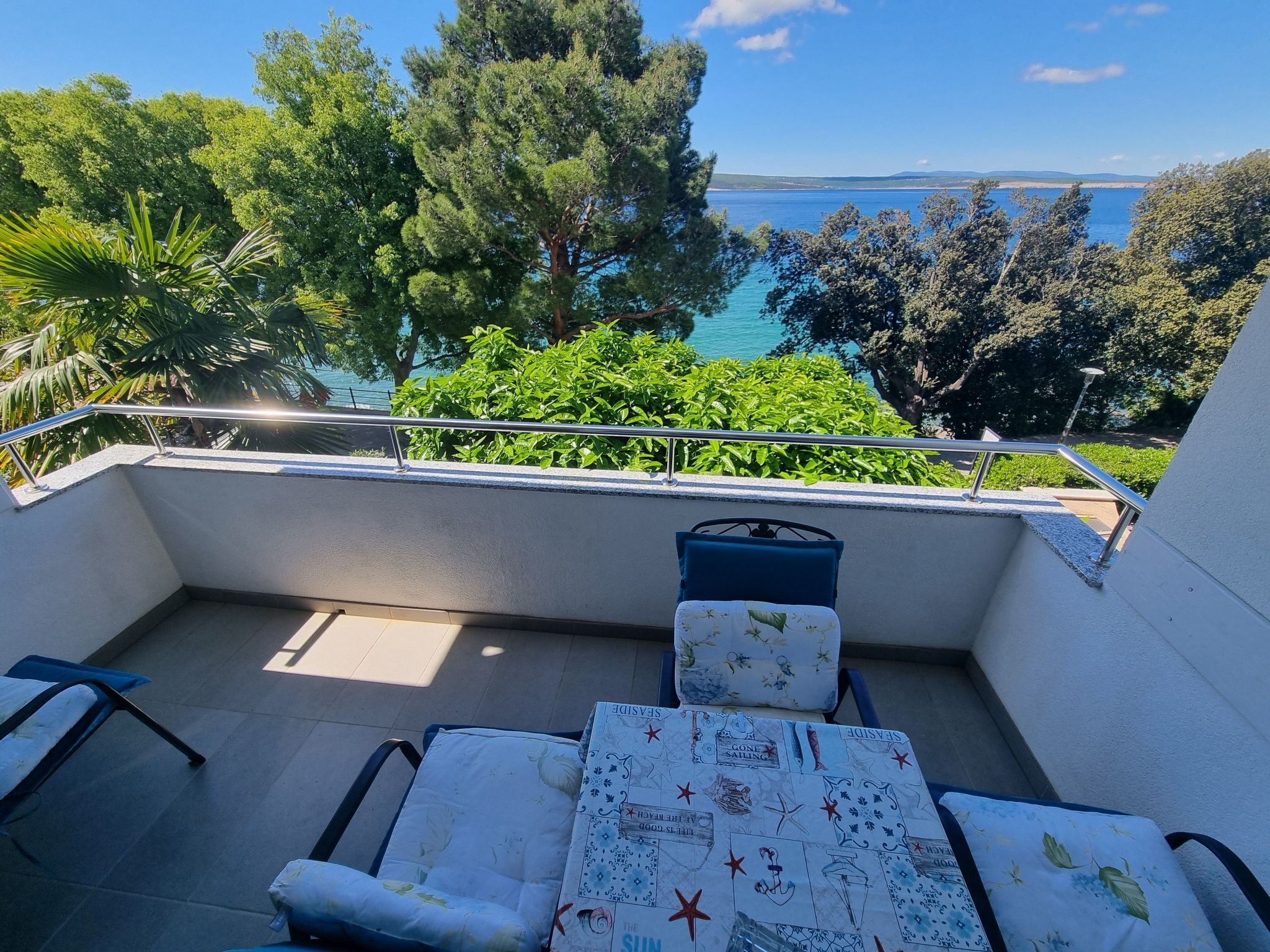 Ein Balkon mit Meerblick, ein Tisch mit Tischdecke im Seestil und ein Stuhl.
