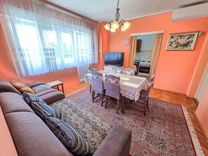 A living room with a sofa, a dining table with chairs, a TV, and a kitchen area visible through a doorway. - Wohnung für 7 Personen, 100m vom Strand by Interhome (Crikvenica)
