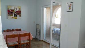 Un comedor con una mesa y sillas de madera, un vidrio que da a un balcón y una mesa pequeña con mantel azul.