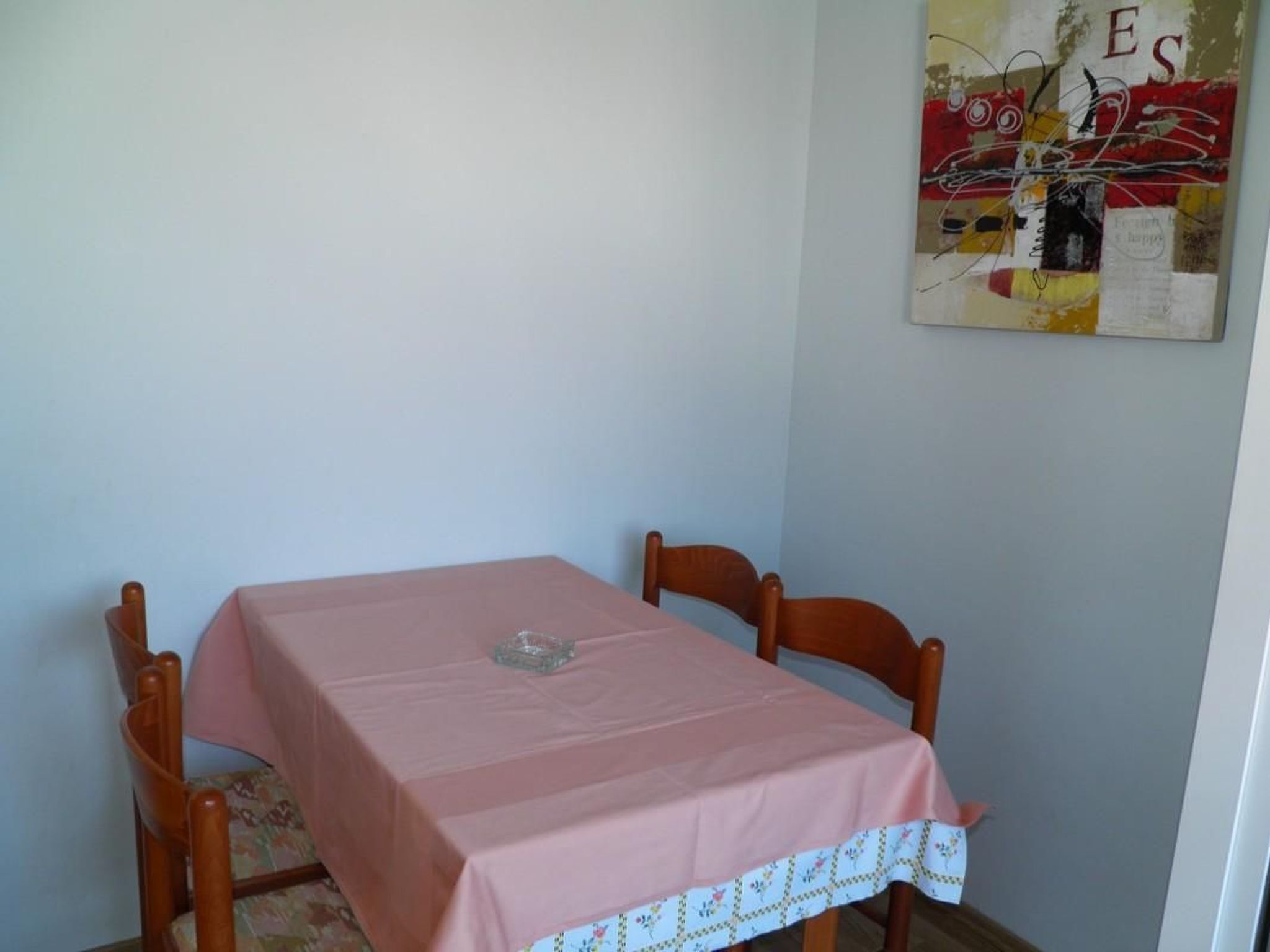 Uma mesa de jantar com toalha rosa, rodeada por cadeiras de madeira.