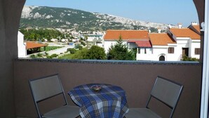 Un balcón con dos sillas y una mesa, con vista a un pueblo con edificios y una montaña.