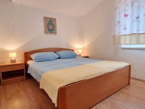 Ein Schlafzimmer mit einem Holzbett, zwei Nachttischen, einer Nachttischlampe, einer Wanddekoration und einem Fenster mit einem Blumenvorhang.