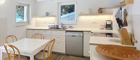 A modern kitchen with white cabinetry, a dishwasher, a coffee maker, and a wooden cutting board.