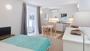 Ett hotellrum med en säng, ett skrivbord, en stol, en tv, en liten köksdel och en skjutdörr ut till balkongen.