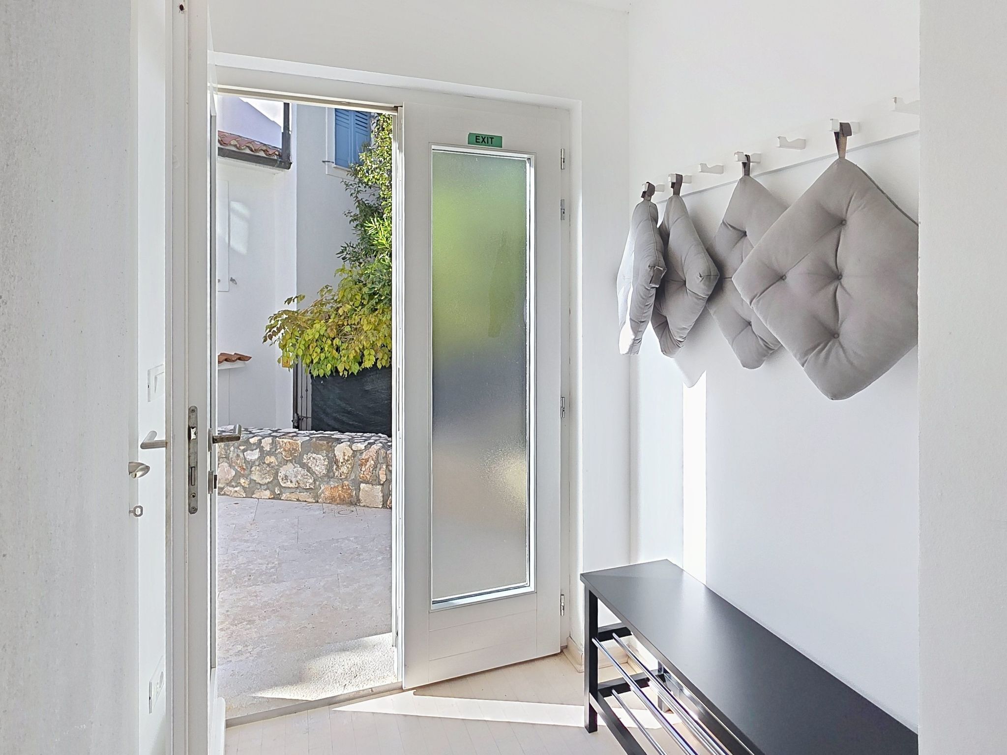 A modern room with a glass door leading to an outdoor area, a black bench, and a wall-mounted cushion.