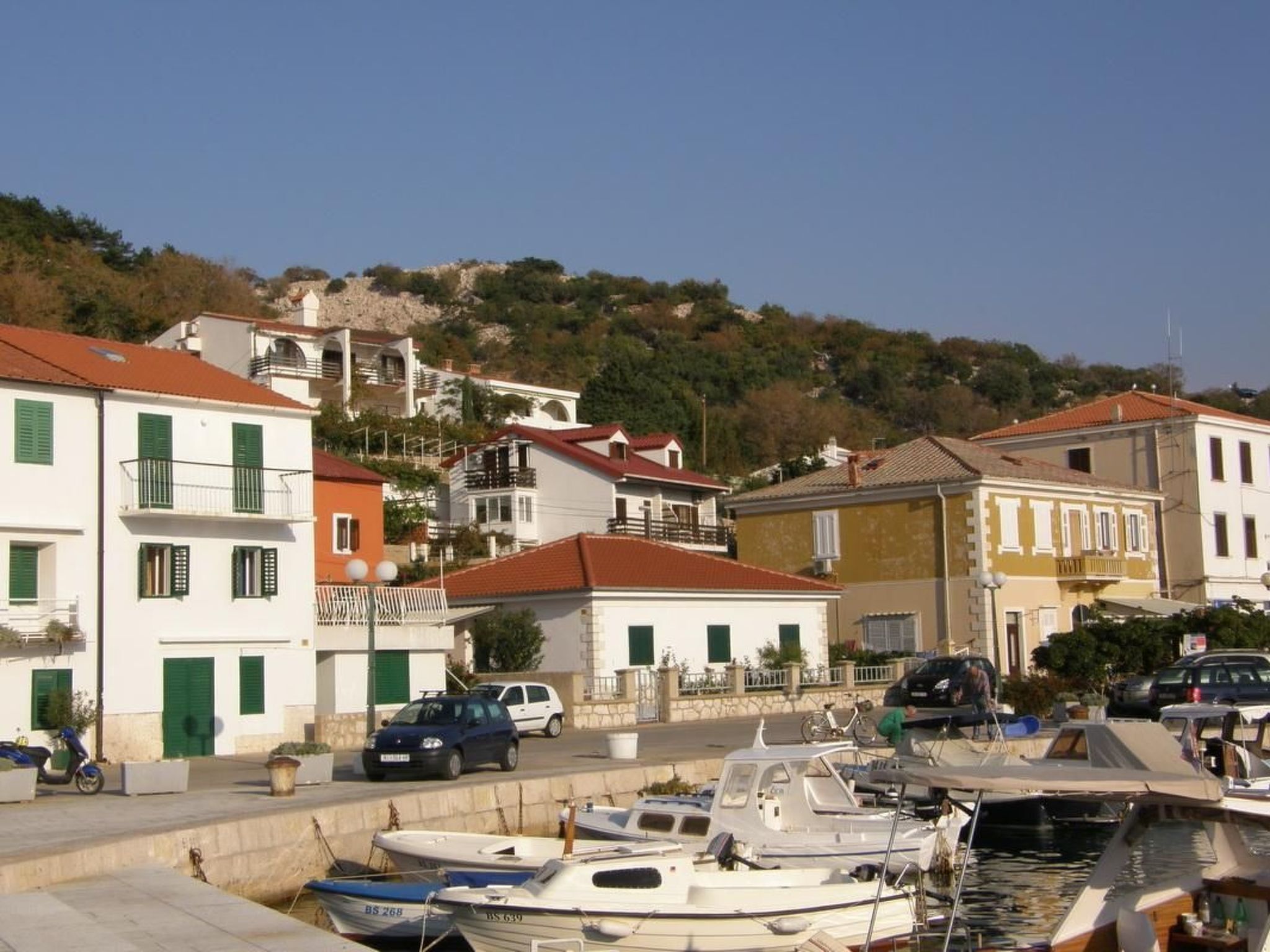 A marina with boats docked, surrounded by buildings with red-tiled roofs and green shutters.