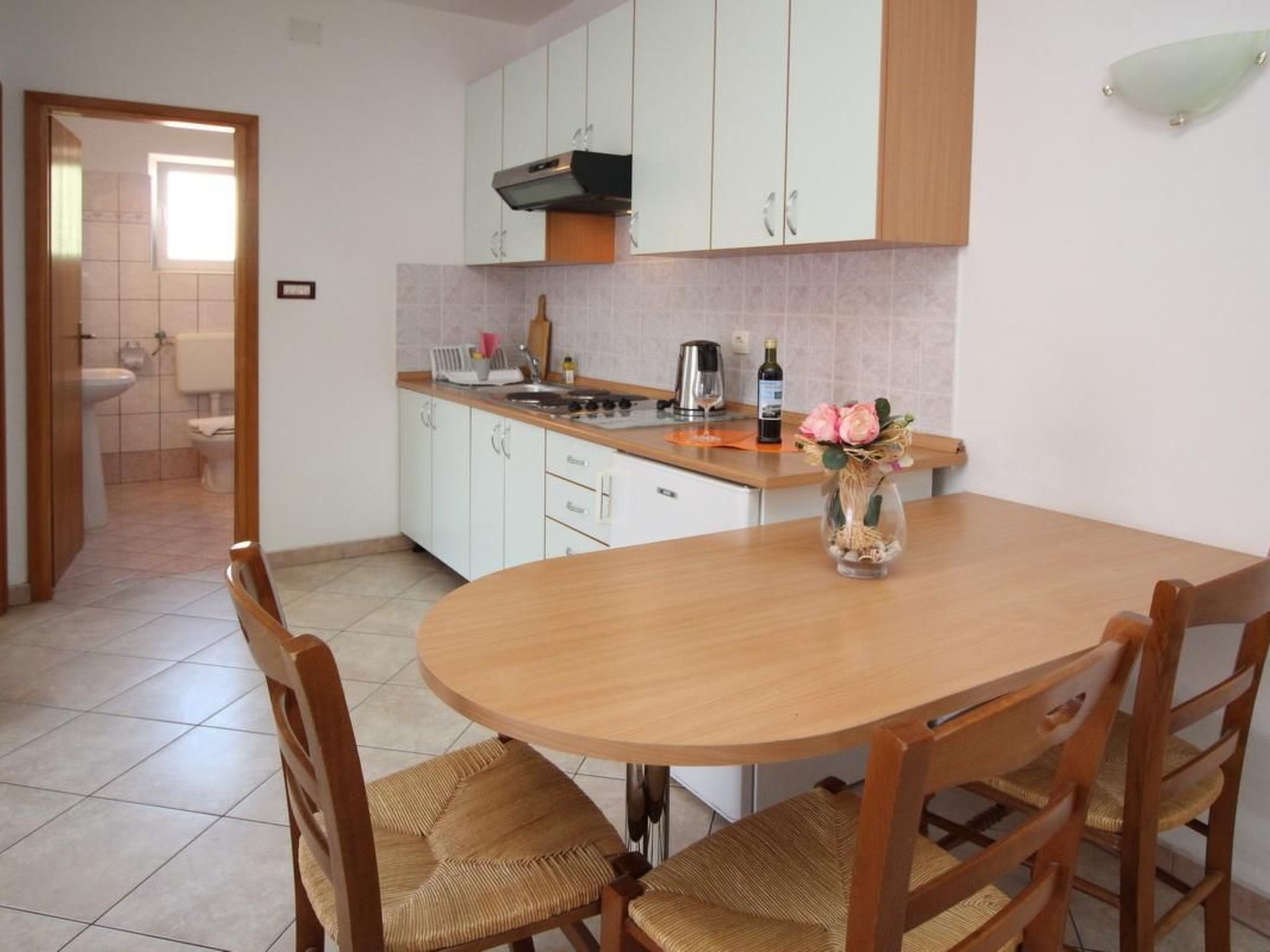 A kitchen with white cabinets, a wooden dining table, and chairs. There is a vase with flowers on the table.