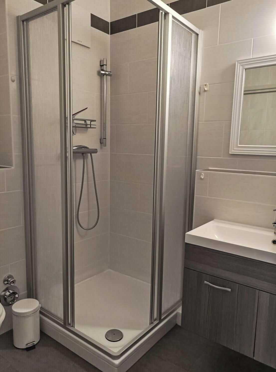 Ein modernes Badezimmer mit einer gläsernen Dusche, einem weißen Waschbecken und einer dunklen Kommode.