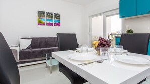 Ein moderner Essbereich mit einem weißen Tisch für zwei Personen, einem grauen Sofa und Blick ins Freie.