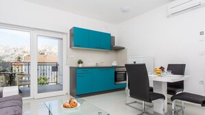 Eine moderne Küche mit türkisfarbenen Schränken, ein Essbereich mit einem Glastisch und ein Balkon mit Blick auf die Hügel.