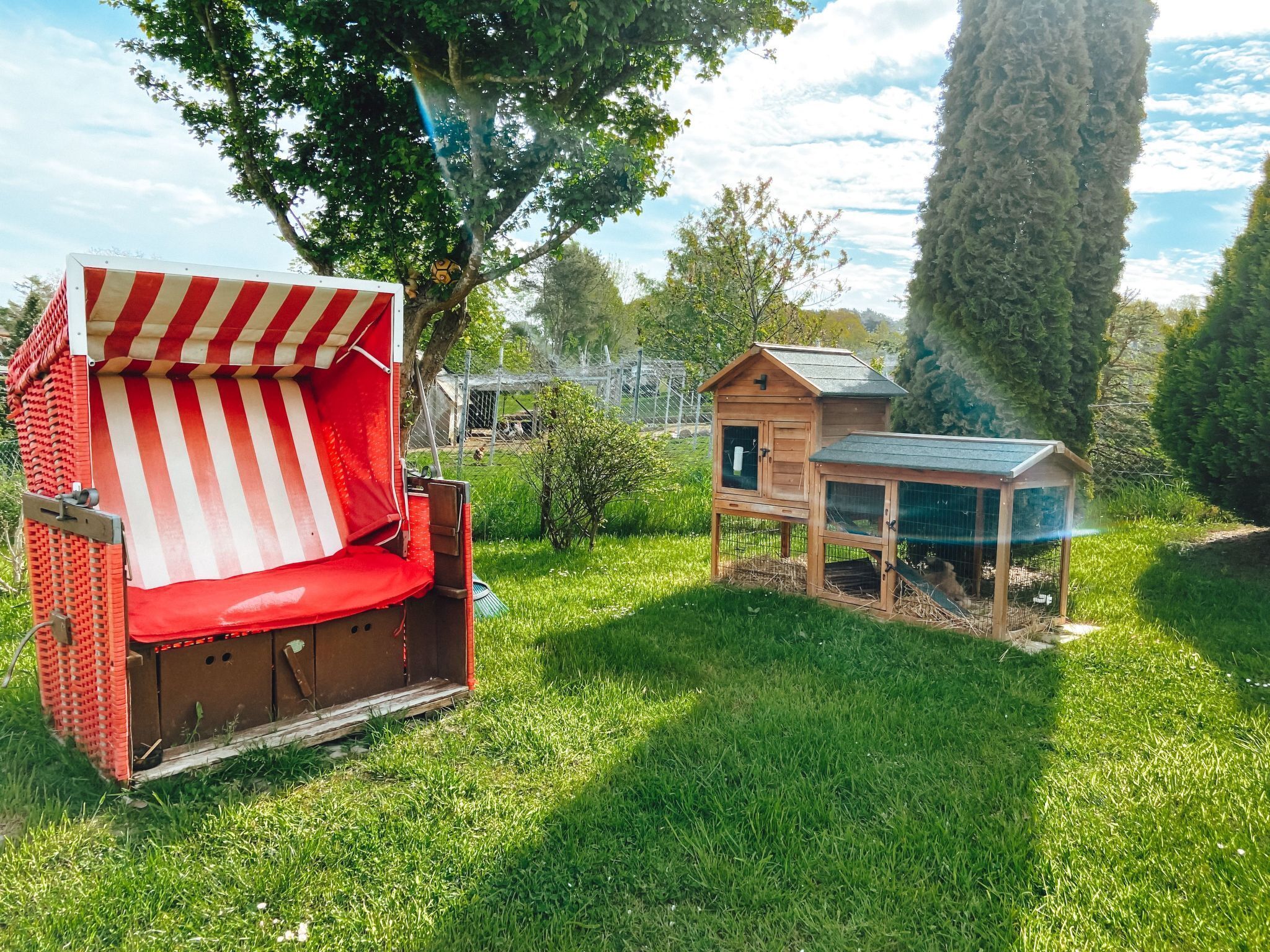 Un espace extérieur aménagé avec des sièges à rayures rouges et blanches, doté d’une structure en bois et d’un petit bâtiment en bois surmonté d’un toit vert.
