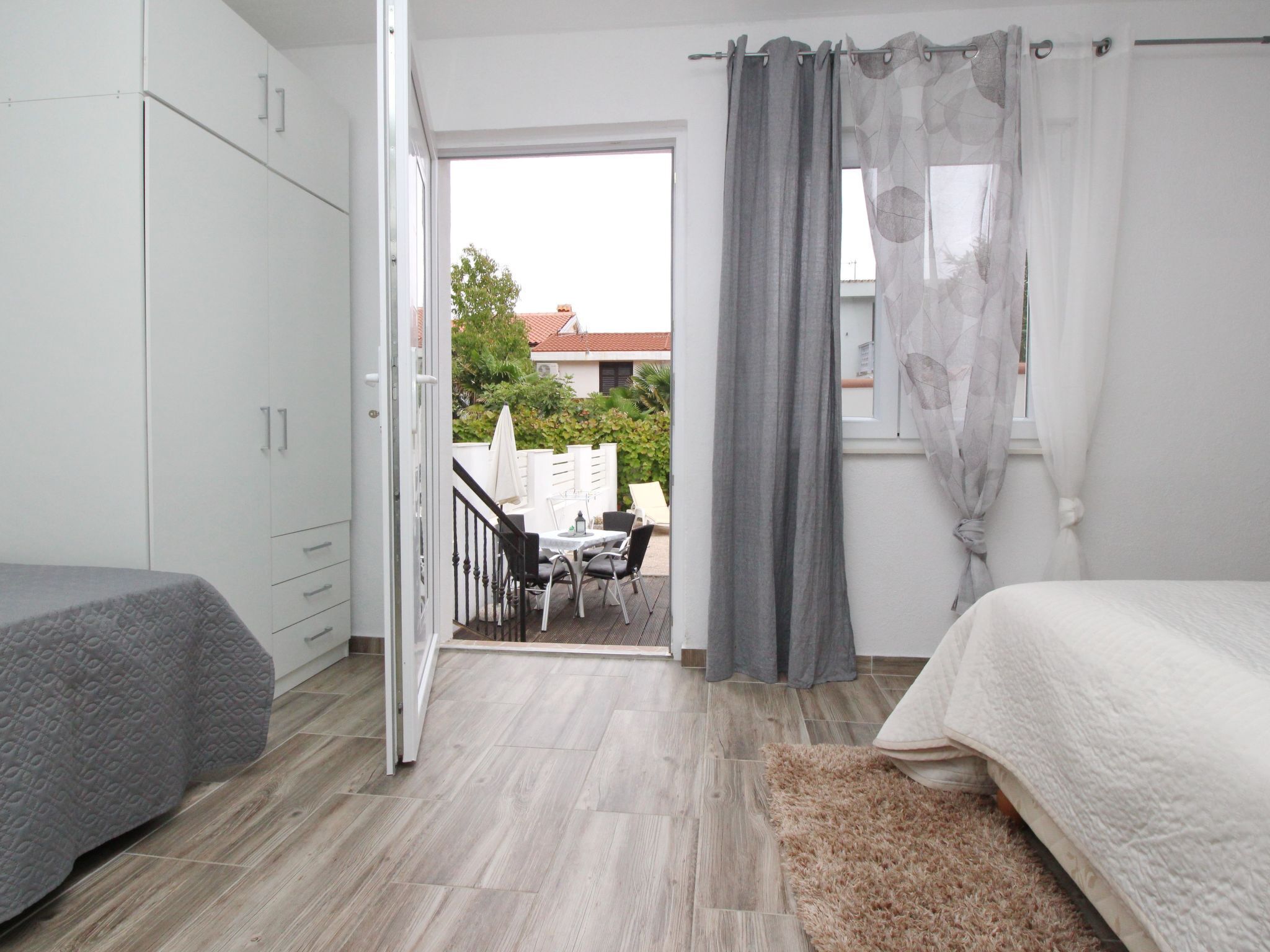 Een slaapkamer met een bed, een bureau en een stoel. Er is een balkon met een tafel en stoelen.