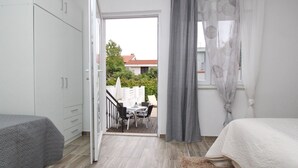 Une chambre avec un lit, un bureau et une chaise. Il y a un balcon avec une table et des chaises.