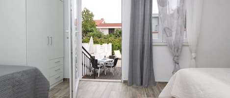 A bedroom with a bed, a desk, and a chair. There is a balcony with a table and chairs.