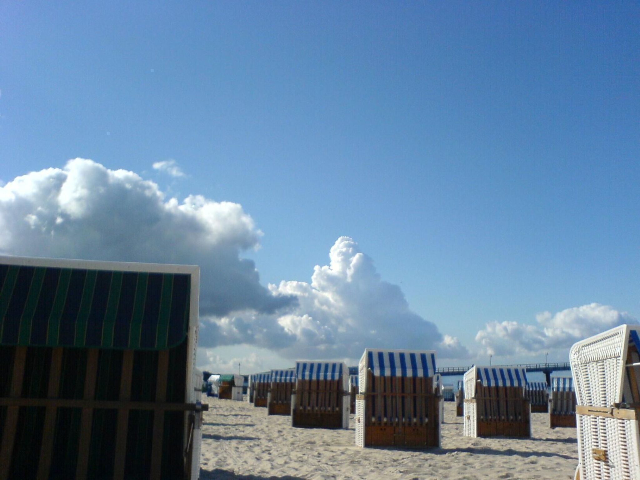 A beach with rows of beach chairs and umbrellas, a wooden fence, and a clear sky with clouds.