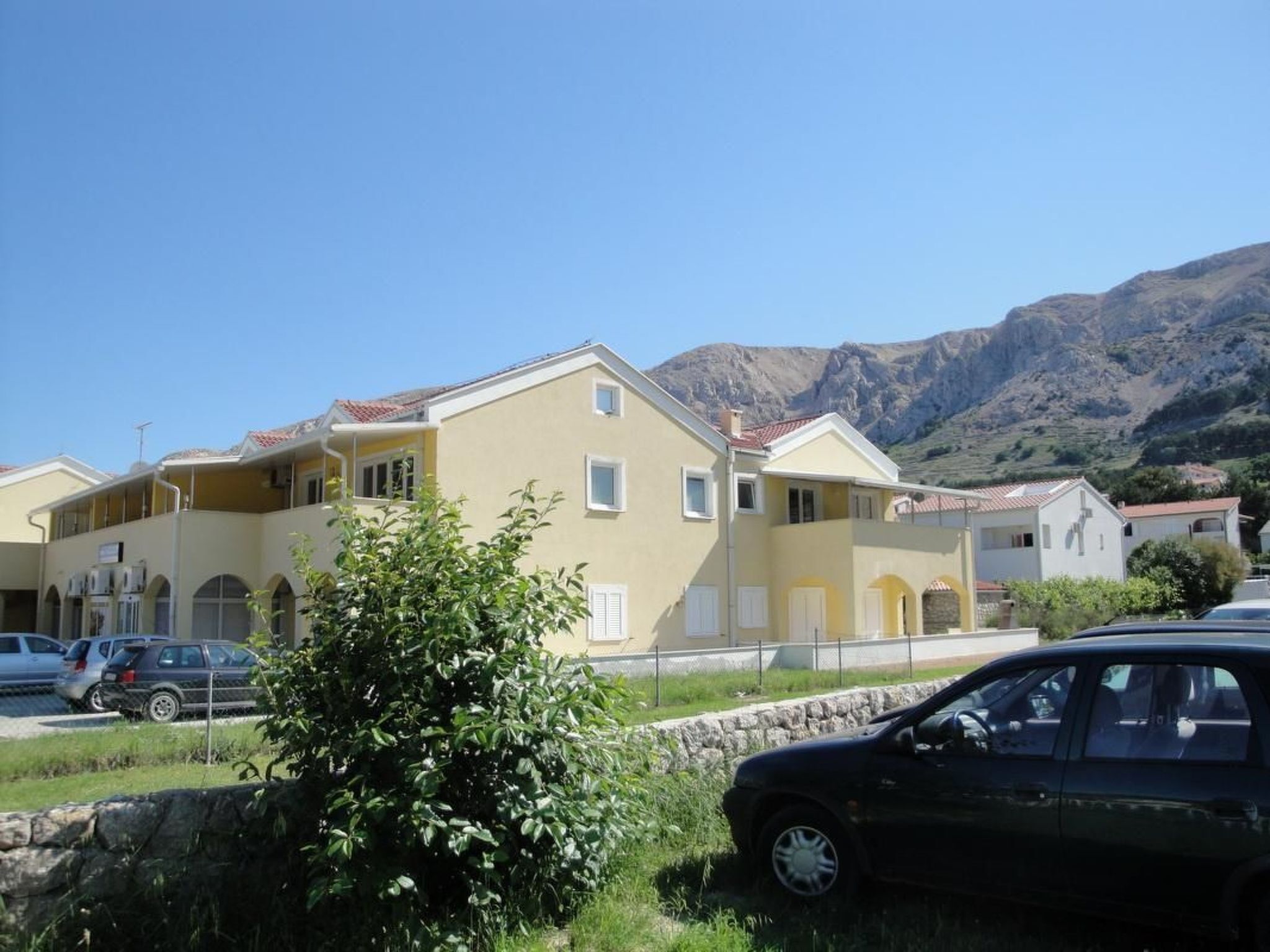 Ein gelbes Gebäude mit rotem Ziegeldach, geparkte Autos und ein Berg im Hintergrund.