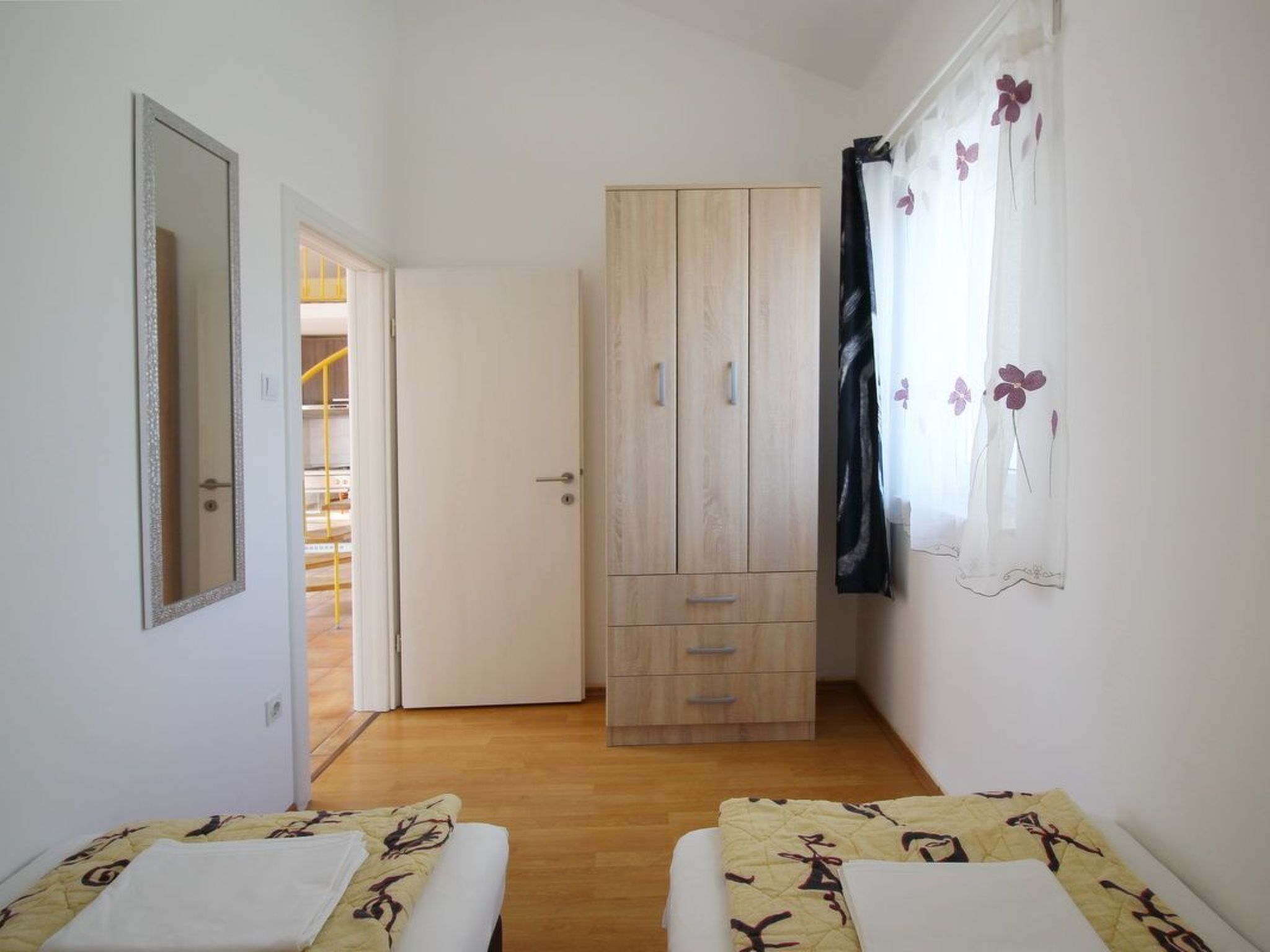 Un dormitorio con dos camas, un armario, un espejo y una puerta que da a un baño.