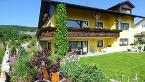 A yellow two-story house with a balcony, surrounded by a well-maintained garden with various plants and flowers. - Fewo im OG mit Balkon by Interhome (Gleißenberg)