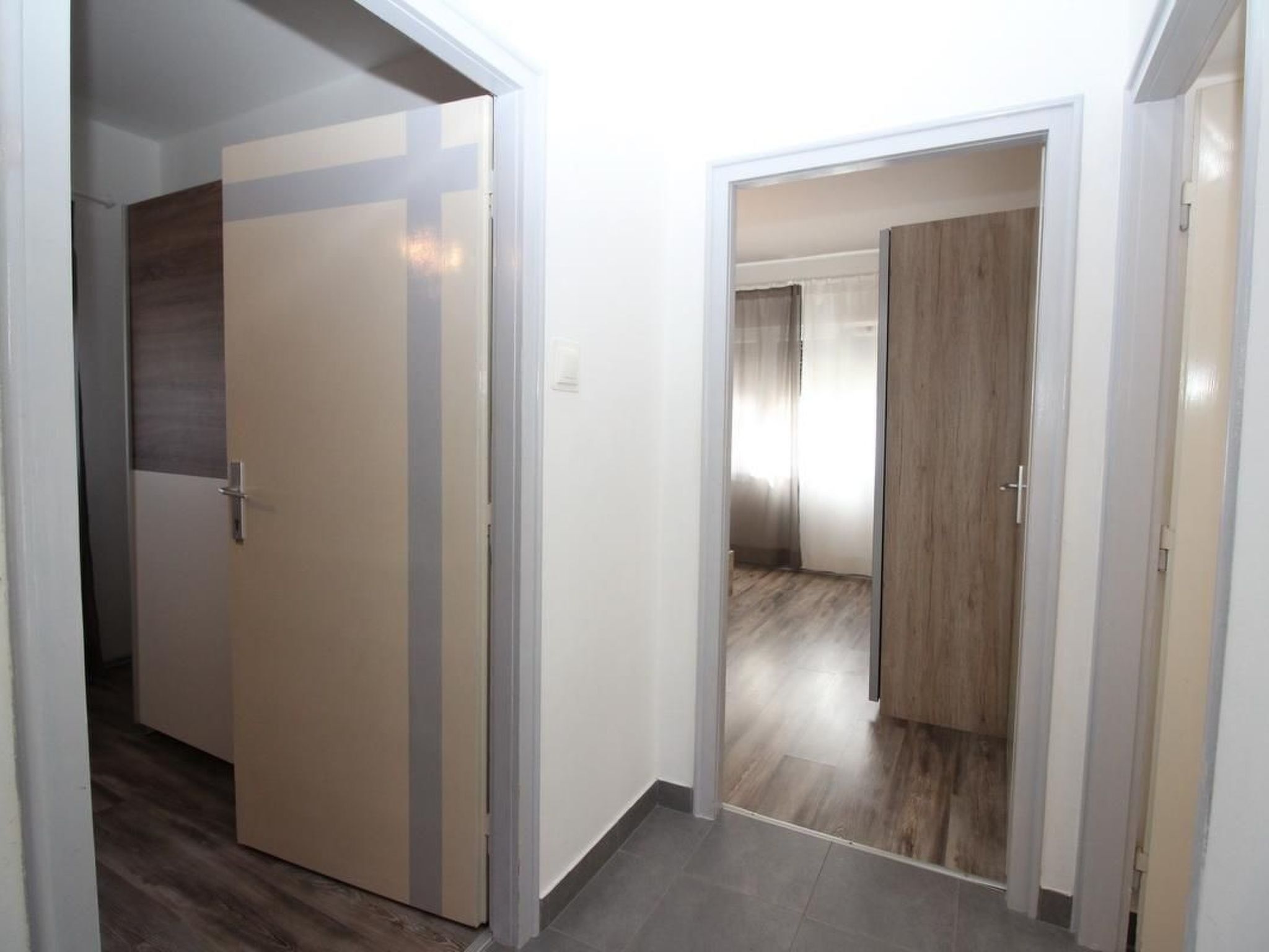 A hallway with a door leading to a room with a wooden floor and a large window.