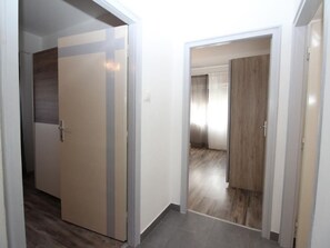 Ein Flur mit einer Tür, die in einen Raum mit Holzboden und einem großen Fenster führt.